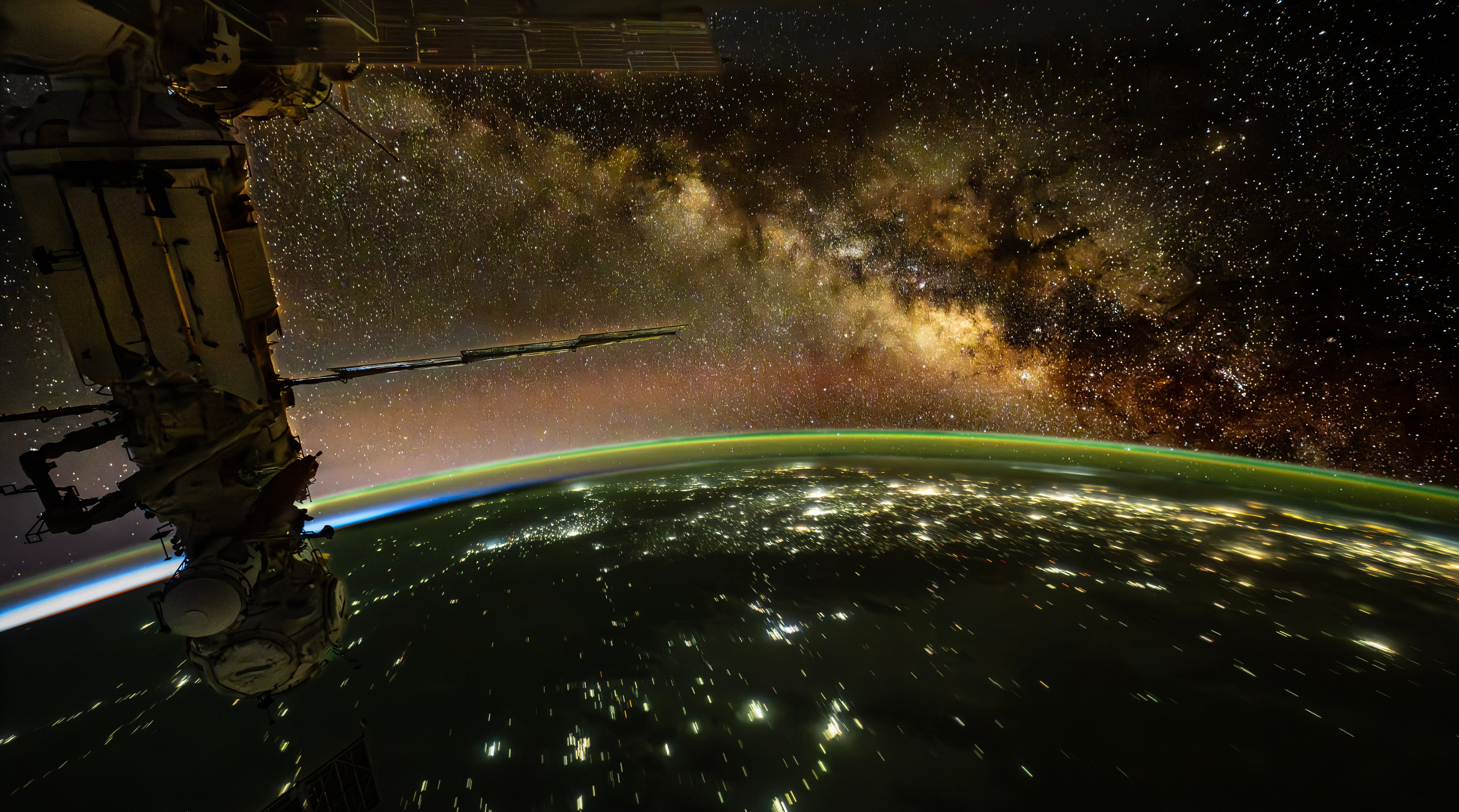 Don Pettit’s view from the International Space Station: human city lights stream across Earth below a green atmospheric rim and the Milky Way above.